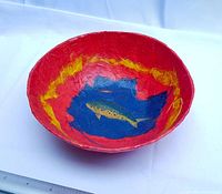 Angled view of handmade bowl showing red exterior and fish painting inside.