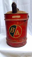Front view of large red metal oil/gas can with British American Oil Company B/A logo and black spouts.