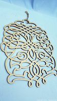 Laser-cut wooden ornament laying flat on a light background showing front detail of intricate carved pattern.