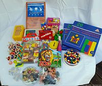 Overall view of lot of vintage toys and trinkets showing multiple boxed toys, containers of marbles and balls, wooden bead sets, and plastic animal figures.