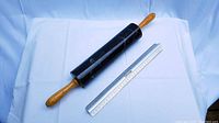 Marble rolling pin with wooden handles shown alongside a metal ruler on a white fabric background for scale.