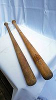 Pair of vintage wooden baseball bats lying on white cloth showing length and condition