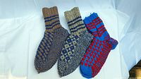 Photo showing three pairs of hand-knitted large wool socks in different colors and patterns