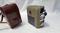 Photo showing the Eumig camera and leather carrying case side by side, highlighting the camera's olive green textured body and chrome lens.