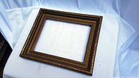 Vintage wooden picture frame lying on white fabric background, photo captured to show full frame and wood texture.