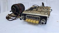 Vintage Philips car radio and electric motor side-by-side on white background revealing front, top, and partial side views.