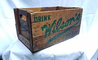Side view showing 'Drink Wilson's Ginger Ale Since 1875' in green paint on natural wood.