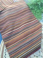 Photo showing the multi-colored striped runner rug with horizontal stripes in brown, orange, yellow, and green hues and tassel fringes.