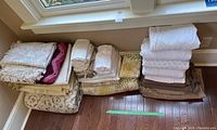 Various folded assorted linens and blankets arranged on floor by window with floral and solid colors