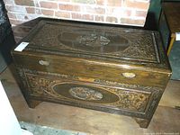 Full view of carved wooden chest with Asian motifs and scenic carvings on front and top.