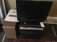 Stack of electronics including Insignia TV on top, speakers on bottom, Sony and Panasonic media devices in middle, and a Harman/Kardon amplifier on top shelf