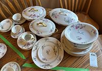 Complete view of set items including plates stacked, cups and saucers, two covered serving dishes with gold handles, and a bowl.