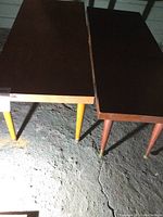 Two rectangular wooden Mid-Century Modern coffee tables seen from above, showing the top surfaces and tapered wooden legs with brass feet.