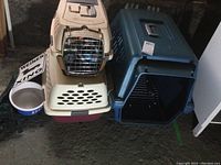 Photo of multiple plastic pet carriers and a large dog bowl on the ground