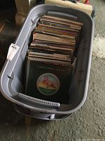 Overview of gray plastic tote filled with a collection of vinyl records, showing some album covers and upright arrangement