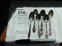 Six sterling silver spoons laid out on white fabric, showing variety of designs and sizes.