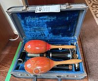 Open clarinet case showing pair of wooden maracas resting on blue velvet lining with clarinet pieces.