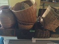 Photo showing various sizes and types of wicker baskets, including a large round basket, a wicker vase, and rectangular baskets with handles placed on a table.