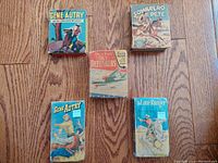 Top down view of five vintage Big Little Books arranged on wooden floor showing front covers of Sombrero Pete, Gene Autry (two editions), Sky Defenders, and The Lone Ranger