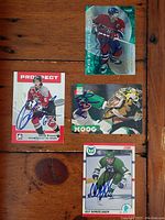 Top-down photo of four autographed NHL hockey cards showing Derrick Brassard, Saku Koivu, Andy Moog, Ulf Samuelsson on wood surface.