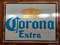 Front view of the wooden plank sign painted with the Corona Extra logo and yellow crown, showing the entire design and condition.