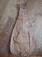 Front view of the tan leather crossbody bag displaying the shoulder strap with rivets and the front flap pocket with snap button.