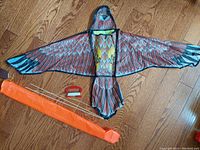 Both kites laid flat showing hawk wing patterns, orange wind sock, and wooden rods on wooden floor.