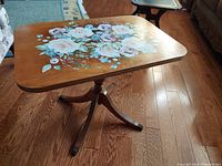 Rectangular oak occasional table with painted floral top and bronze clawfoot legs, seen from side angle.