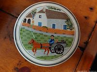 Top view of the porcelain container lid showing the detailed hand painted scene of a horse and cart, man, and houses in the background.