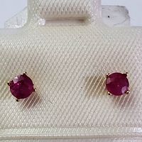 Front-facing close-up of two round red ruby stones set in four-prong gold mounts on a white display pad
