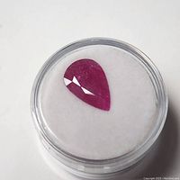 Pear-shaped genuine ruby gemstone inside a clear display container on a white background.