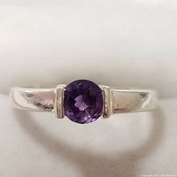 Close-up of the silver ring with a round faceted amethyst gemstone in the center.