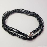 Multi-strand black spinel necklace with silver lobster clasp laid in a circle on a white background.