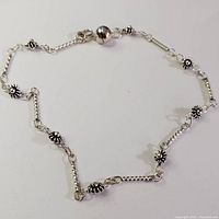 Image showing the full length of the silver bracelet laid flat, displaying floral design elements and bell charm.