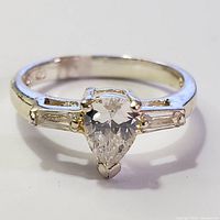 Front view of silver ring with pear-shaped cubic zirconia center and baguette side stones.