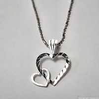 Close-up of silver heart pendant necklace showing faceted detailing and interlocked heart design