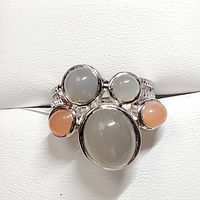 Front view of sterling silver ring with a large central grayish-white moonstone, two smaller grayish-white moonstones, and two peach moonstones on a white background.