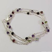 Full view of coiled 36 inch silver necklace with bezel set multi-color gemstones: amethyst, garnet, and peridot.