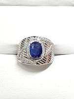 Front view of silver ring with deep blue oval sapphire center stone and clear round accent stones on textured ribbed band.