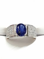 Front view of silver men's ring showing central oval blue sapphire and adjacent cubic zirconia stones.