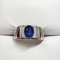 Front view of the men's silver ring showing the oval blue sapphire center and surrounding cubic zirconia stones against a white background.