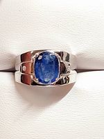 Front view of men's silver ring with central rough-cut oval sapphire and side cubic zirconia stones on a polished band.
