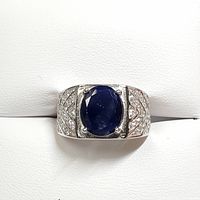 Men's silver ring front view with prominent deep blue oval sapphire center stone and cubic zirconia accents on the band.