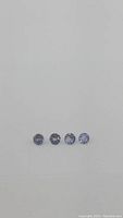 Four round-cut tanzanite gemstones arranged in a row on a white background, showing color and cut detail.