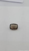 Front-facing photo of a large cushion cut smokey quartz gemstone on a plain white background showing the stone's size and facet details.