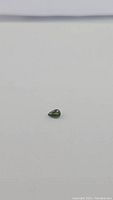 Small pear cut green sapphire gemstone on white background, showing size and shape.