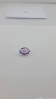 Natural oval cut pink purple amethyst gemstone placed on white background, showing faceted oval shape and bright luster.