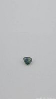 Natural pear-shaped green and blue sapphire gemstone against a neutral background showing color and facets.