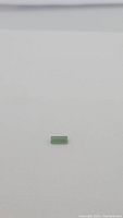 Clear image showing small rectangular green baguette cut tourmaline gemstone against white background