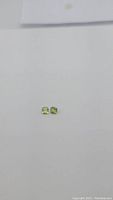Two natural apple green peridot stones, cushion checkerboard cut, shown side by side on a plain white background for size and color comparison.